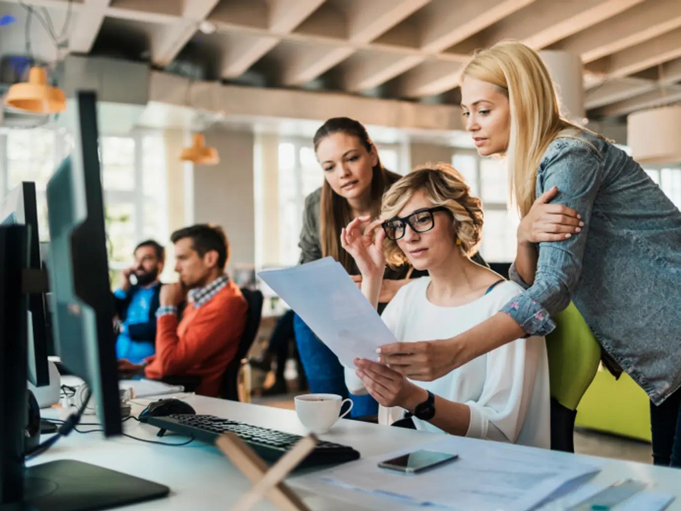 オフィスでコンピューターの画面を見ている人々のグループがいます。